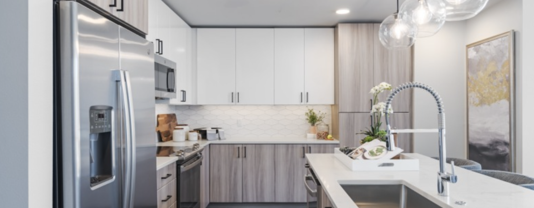 Modern kitchen with stainless steel appliances, white countertops, pendant lights, and wood-accented cabinets.